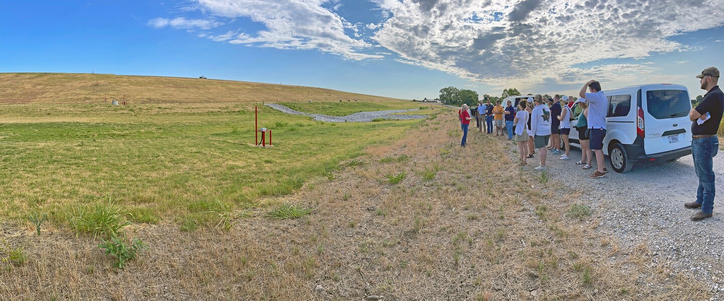 a group of people standing below a dam around cars talking