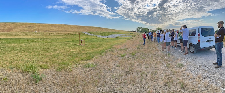 a group of people standing below a dam around cars talking