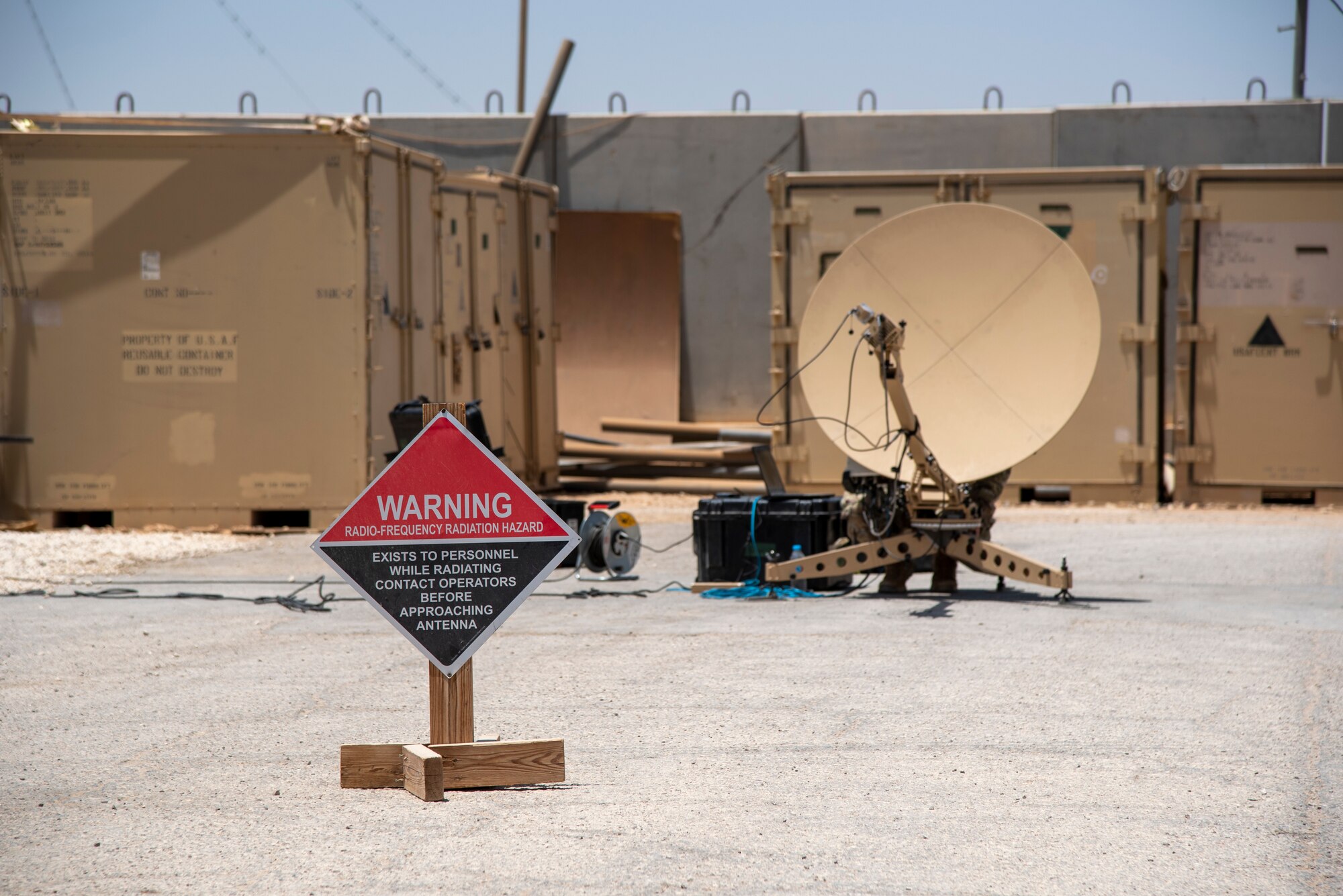 A sign and cordon warn onlookers to stay back from a Communications Fly Away Kit at an undisclosed location, July 20, 2022. The CFK enables the 332d Air Expeditionary Squadron to operate in remote locations by establishing secure communications via satellite. The front of the dish emits high levels of radio frequency radiation. (U.S. Air Force photo by: Tech. Sgt. Jim Bentley)