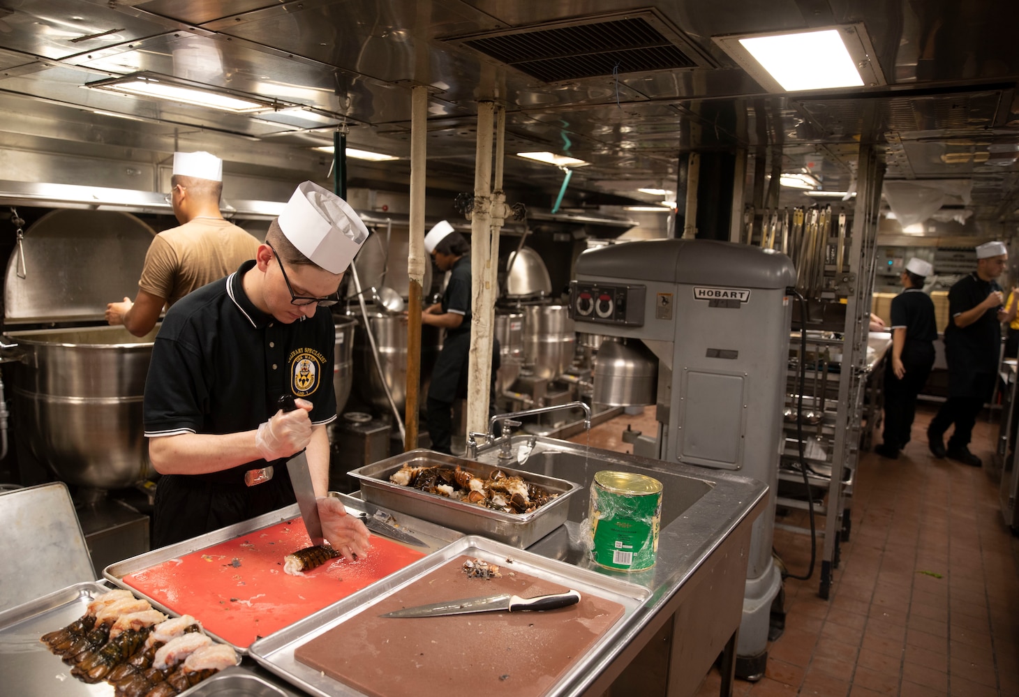 Sailor prepping lobster tail in galley.