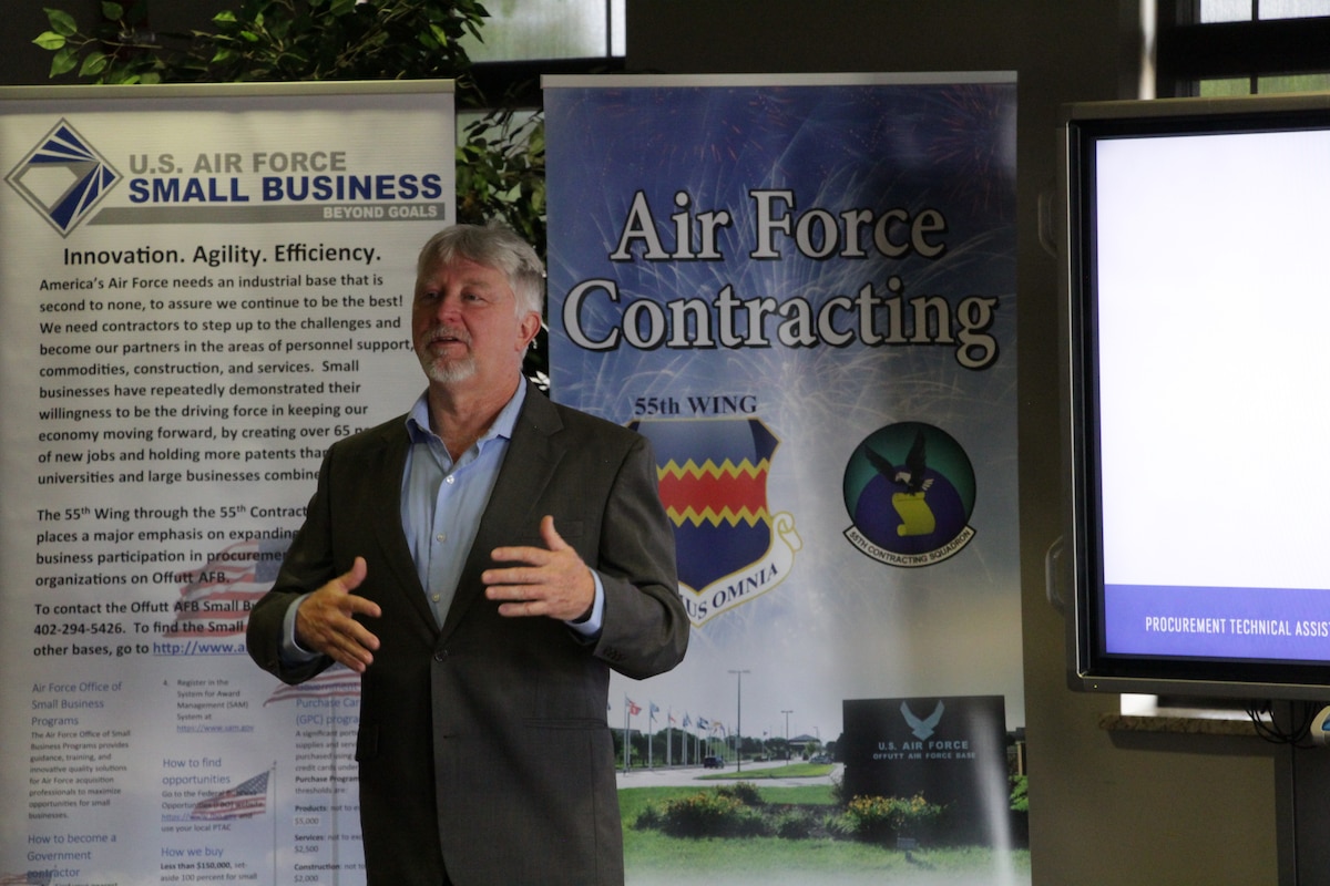 Man speaking while standing in front of two banners about Air Force contracting and small business