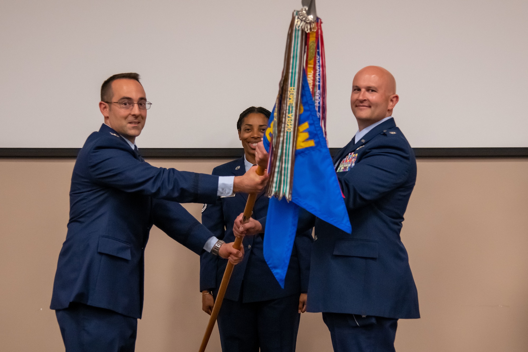 Col. Campanile and Lt. Col. Hendrix each hold onto a guidon flag. Senior Master Sgt. Jones stands between them.