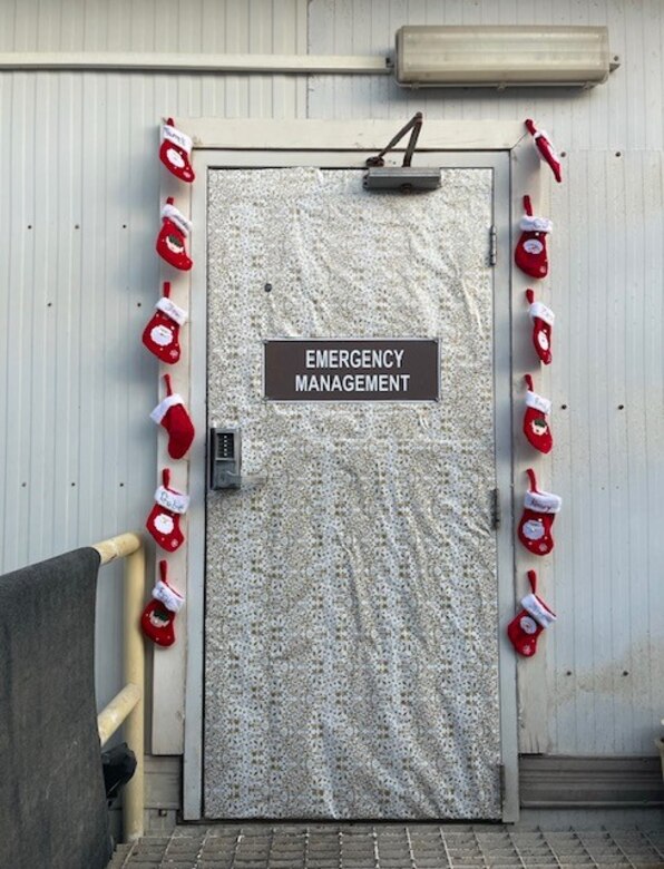 A door is decorated in a Christmas theme with silver paper and a string of stockings hanging from the left and right side of the door.