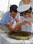 NAVAL STATION NORFOLK (Aug. 5, 2022) Lt. Alisa L. Harl, chaplain aboard the guided-missile destroyer USS Laboon (DDG 58), right, baptizes Blaze Michael Laboon, the great-great-grandnephew of Laboon’s namesake, center. Shipboard bell baptisms are a centuries-old tradition, and several members of the Laboon family have been baptized in the ship’s bell. (U.S. Navy photo by Mass Communication Specialist 1st Class Jacob Milham)