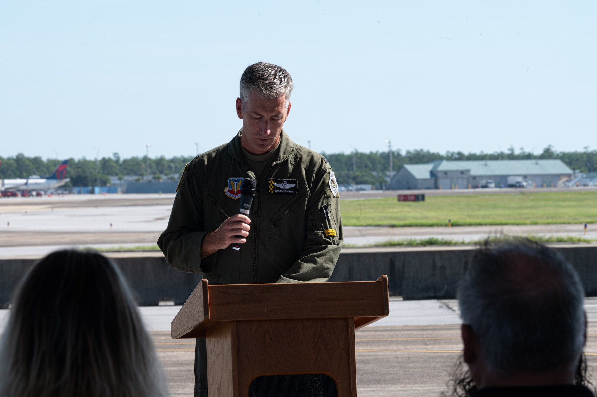 A man in a flight suit gives a speech at a podium.