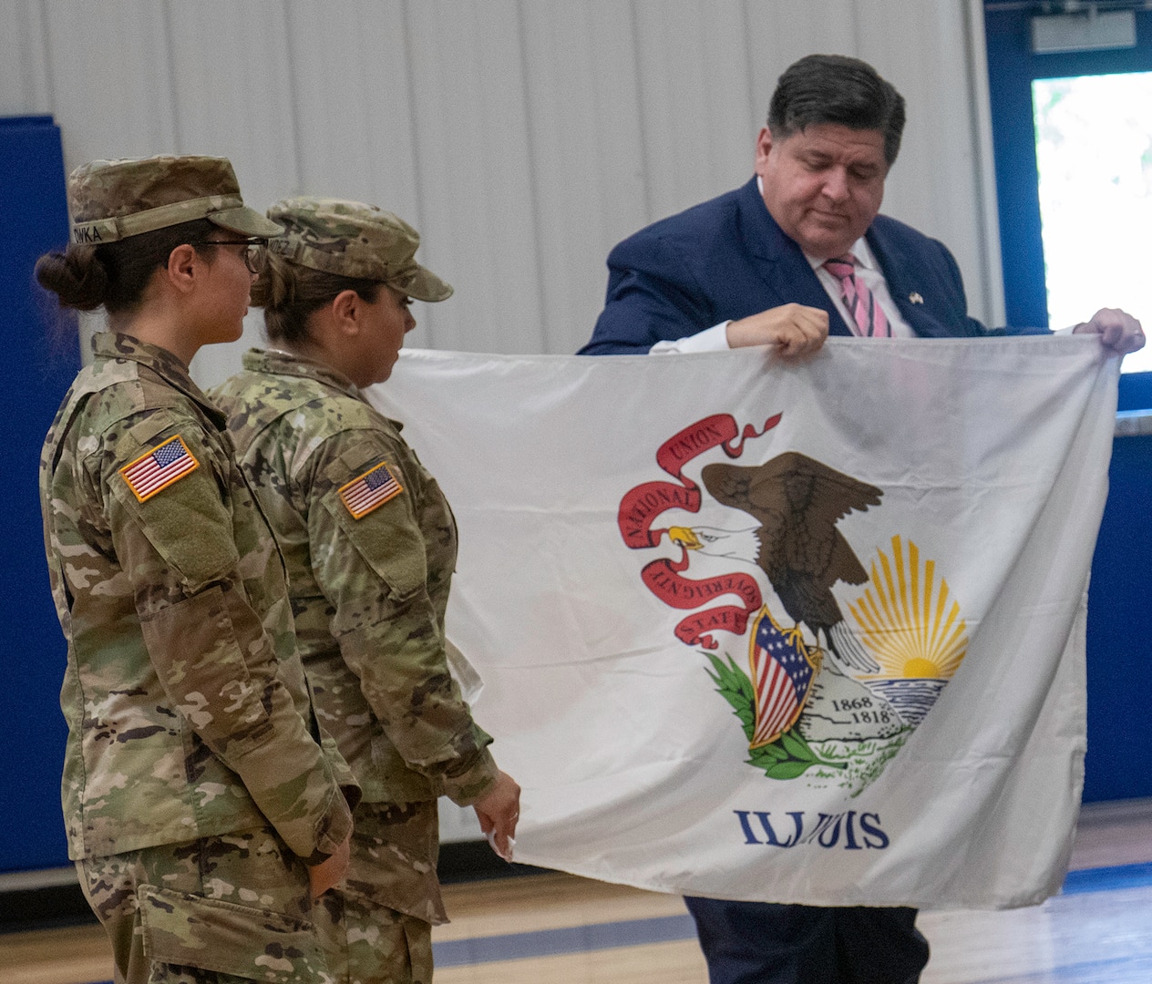 Illinois Governor JB Pritzker presents a state of Illinois flag to Maj. Karen Hernandez, of Bensenville, Commander of the 709th Medical Company Area Support, based in Bartonville, during the deployment ceremony Aug. 6 at Monroe Elementary School in Peoria.