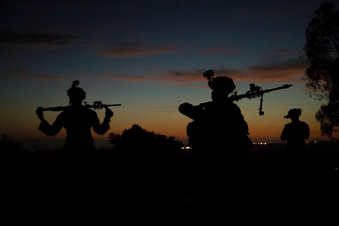 Marines holding weapons stand near each other in the dark as shown in silhouette.