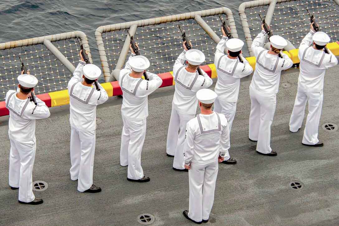 Sailors standing in a line fire weapons aboard a ship at sea.