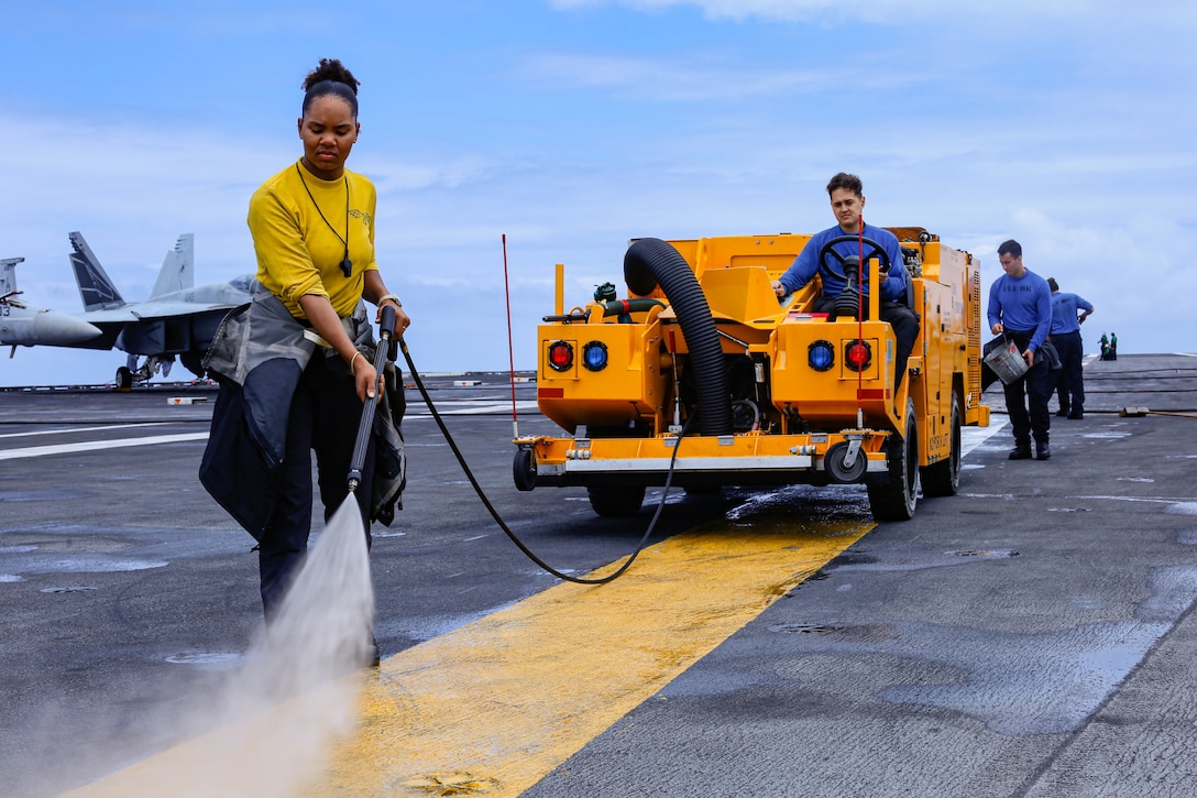 Sailors use a hose to power wash the flight deck of an aircraft carrier.