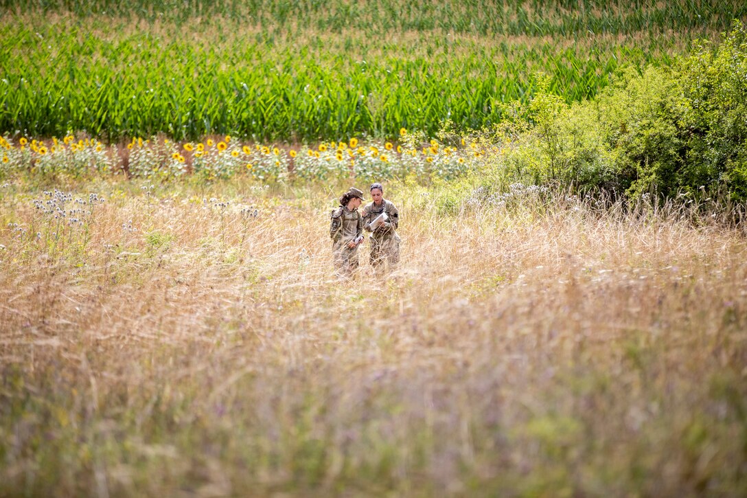 Two service members stand in a field and check their map.