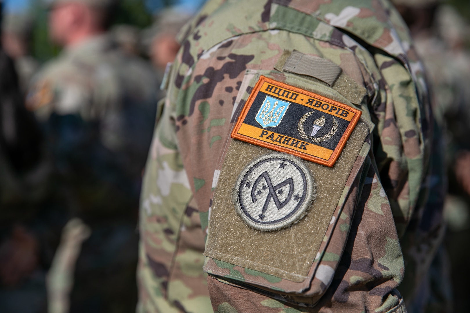 A U.S. Army Soldier assigned to Task Force Orion, 27th Infantry Brigade Combat Team, New York Army National Guard, wears the Combat Training Center-Yavoriv Advisor patch above the 27th IBCT patch during the Joint Multinational Training Group-Ukraine Transfer of Authority ceremony in Grafenwoehr, Germany, August 8, 2022.