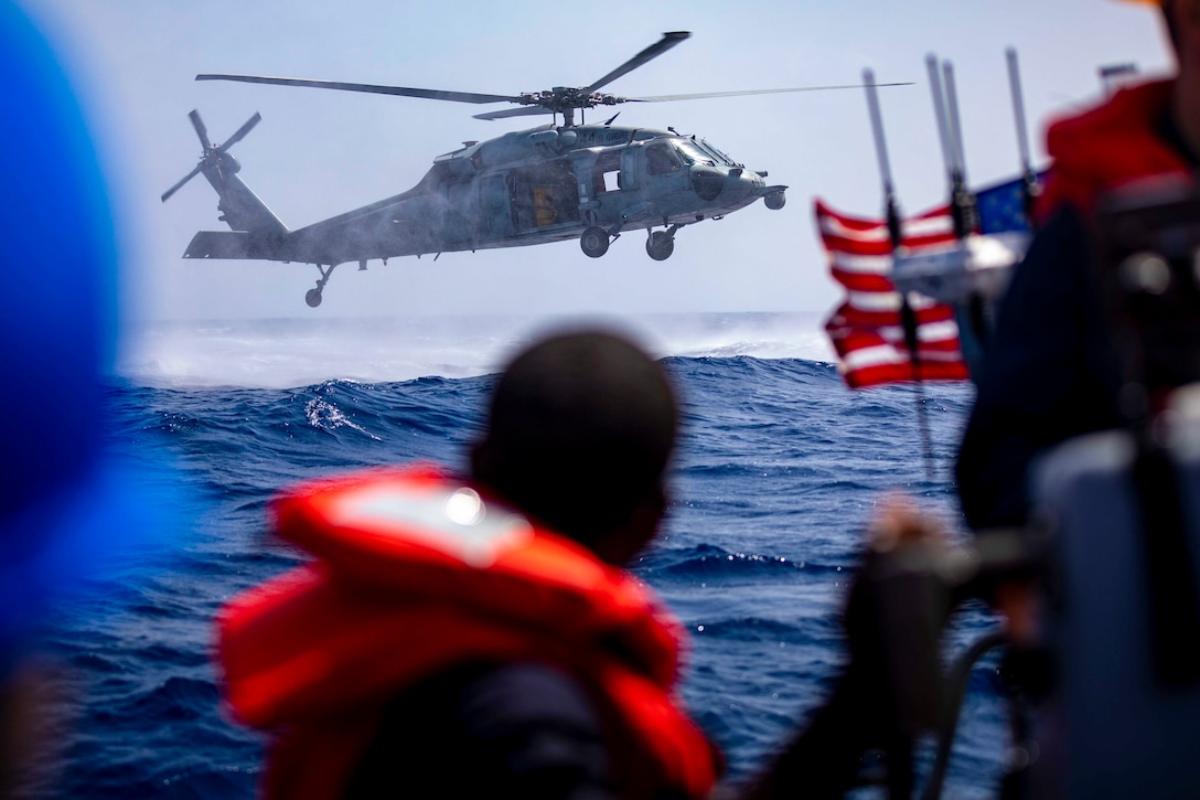 Sailors look out at a helicopter hovering over the ocean.