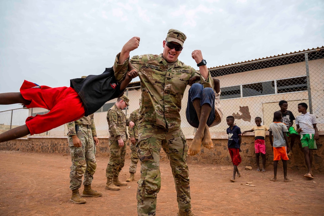 A soldier lifts two children by the forearms.