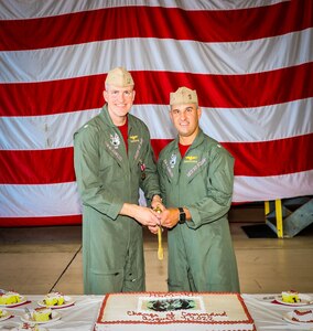 Two officers posing for a photo before ceremoniously cutting a cake with a sword