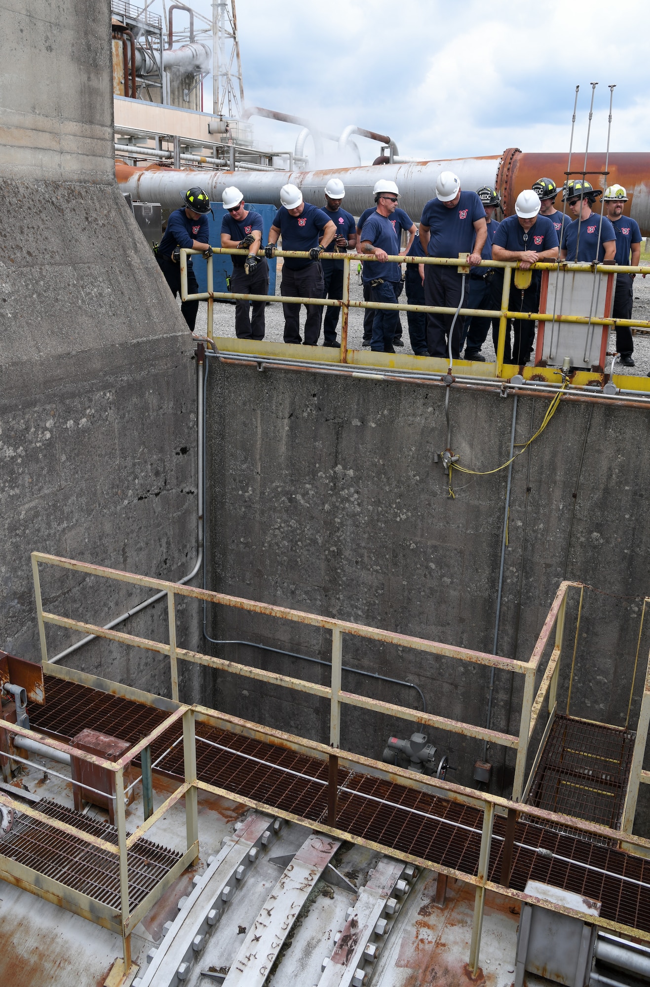 Multiple firefighters standing next to railing overlooking a pit