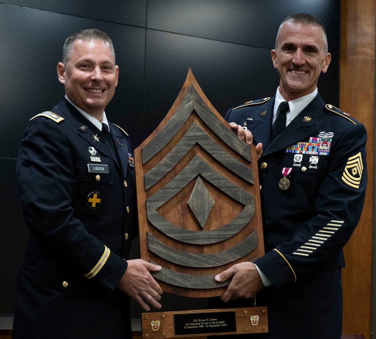Lt. Col. Mark Lueken, who serves as the deputy G-6 during drill status duty, presents Illinois Army National Guard 1st Sgt. Ryan Crews of Mount Vernon, Illinois, a wooden wall plaque in honor of Crews’ more than 34 years of military service at the retirement ceremony Aug. 7 at the Illinois Military Academy, Camp Lincoln, Springfield.