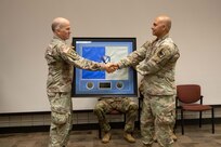 To soldiers shake each others hand while holding a shadow box .