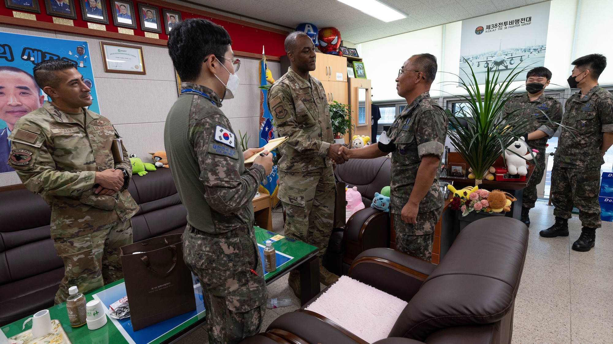 Military members sit together in a room, two are shaking hands.