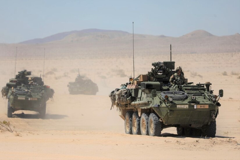 Military vehicles move through desert terrain.