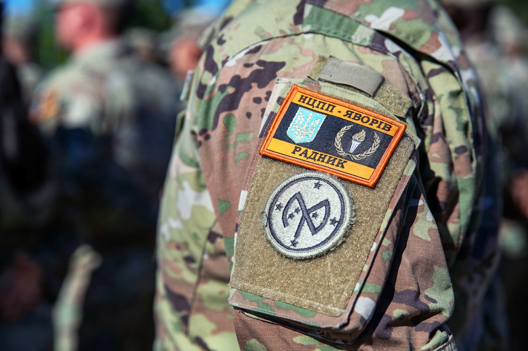 A soldier wears two patches on their shoulder, one of which contains Cyrillic lettering.