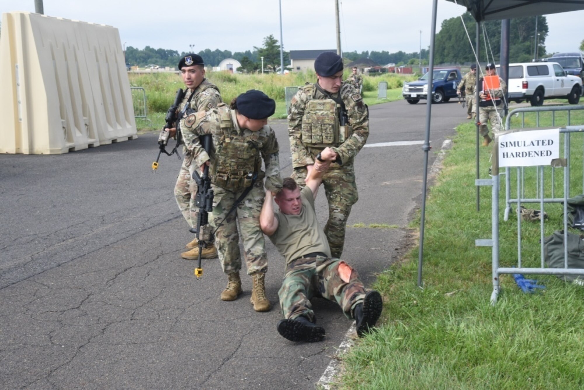 Three military personnel in uniform pull a simulated casualty to safety.