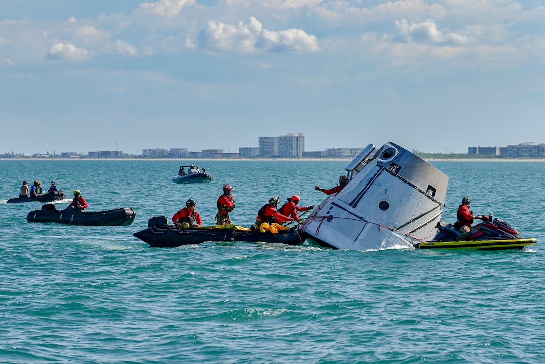 Airmen in rafts surround a space capsule floating in the water.