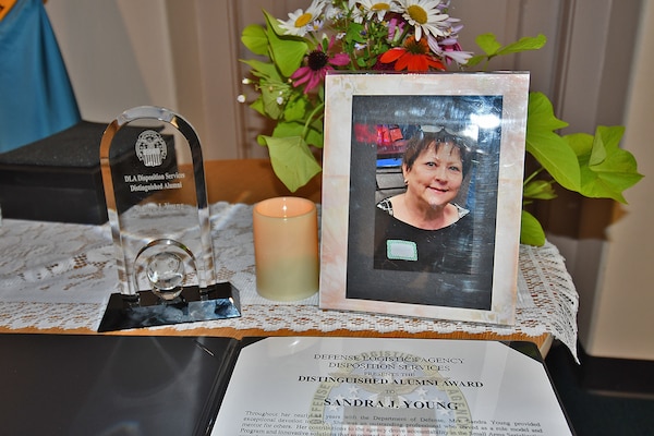 Flowers, a photo, an award citation and a plaque sit on a table with a candle.