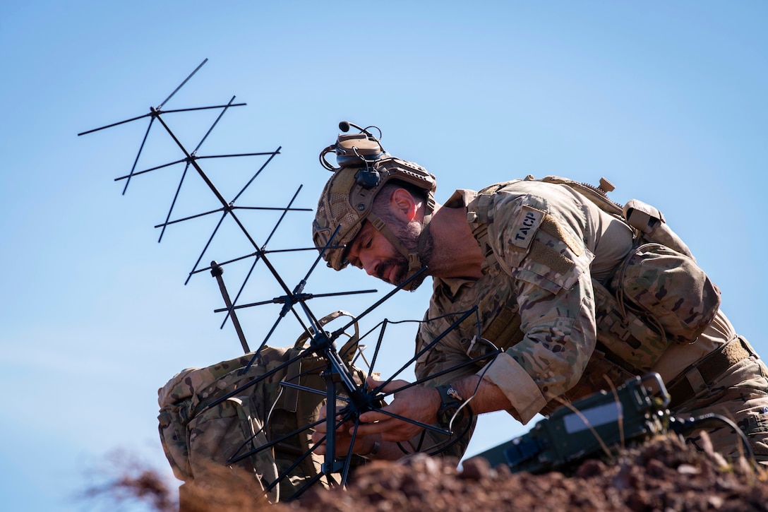 An airman sets up a satellite in a field.