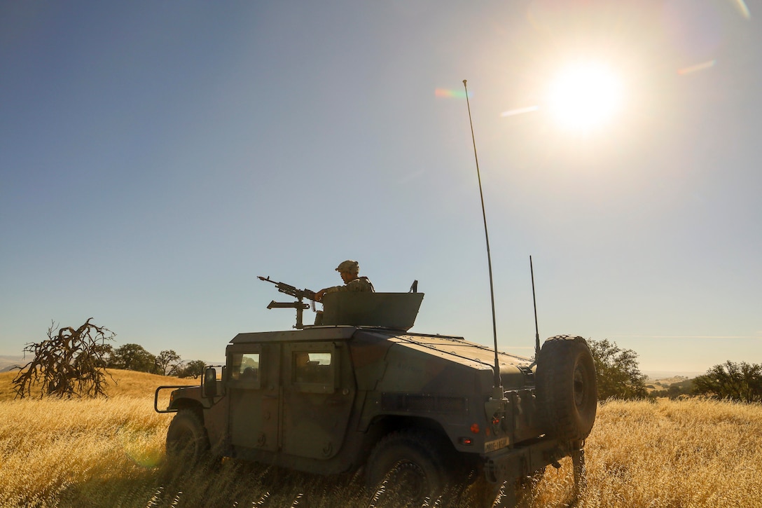 A soldier aims a weapon from a military vehicle in a field.