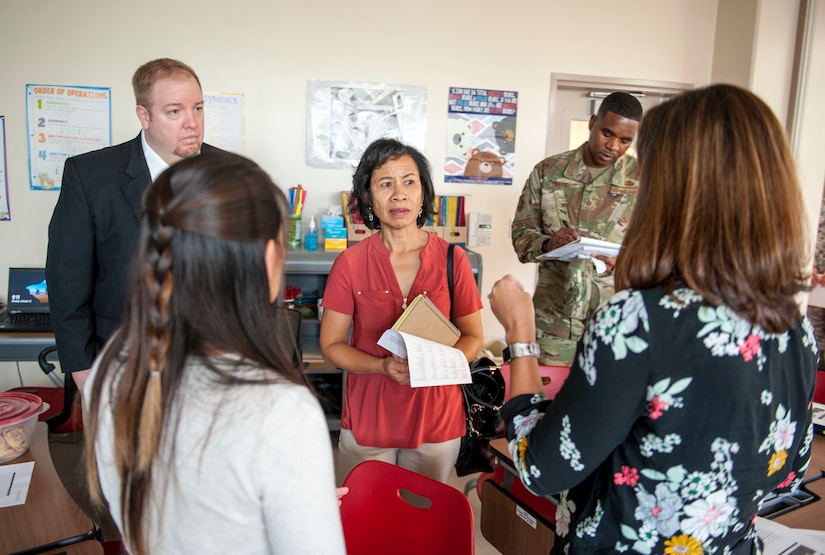 A group of people meet and converse in a classroom.