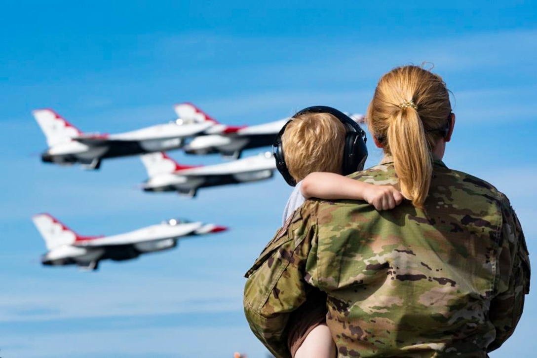 A service member holds a child while watching aircraft fly.