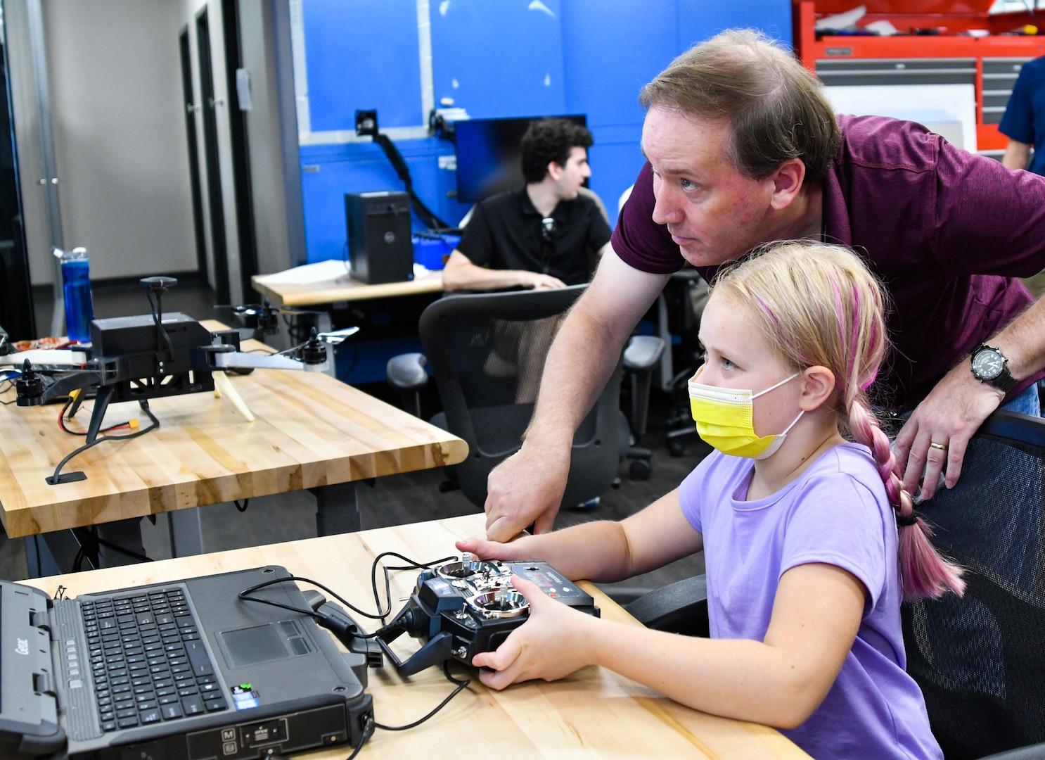 IMAGE: Weapons Control and Integration Department Mechanical Engineer Ian Shafer helps Eliana Shipley, 9, pilot a virtual reality-based drone during the Bring Your Child to Work Day event, Aug. 2. The department demonstrated various 3D printing technologies and how they allow for rapid prototyping of unmanned aerial systems.