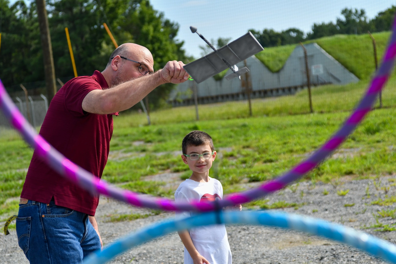 IMAGE: Strategic and Computing Systems Department Engineer Geoff Bland helps his son Miles, 7, launch their 3D-printed rubber band-powered airplane at a pair of target hoops at the Weapons Control and Integration Department’s station. The station was one of many activities available to the children of Dahlgren personnel during the Bring Your Child to Work Day event Aug. 2.