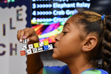 IMAGE: Makiyah Batts, 9, balances dice on a popsicle stick during a game of “Crocodile Crunch” at the Integrated Combat System Department’s Crazy Cost Carnival during the Bring Your Child to Work Day event held at Naval Support Facility Dahlgren, Aug. 2. The department’s Cost and Engineering Branch provided several carnival-like games to test the children’s cost estimating and scheduling skills.