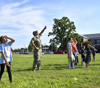 IMAGE: Naval Surface Warfare Center Dahlgren Division’s  Commanding Officer Capt. Philip Mlynarski looks to the sky as water bottle rockets are launched from the parade field by teams of kids Aug. 2. The Integrated Engagement Systems Department hosted the “Blast Off!” station to demonstrate the physics of rocket operations. The station was one of the many activities available to the children of base personnel during the Bring Your Child to Work Day event.