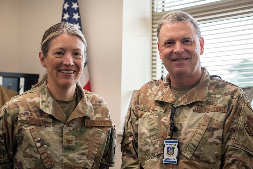 Two military members stand next to each other and pose for a photo inside of an office.