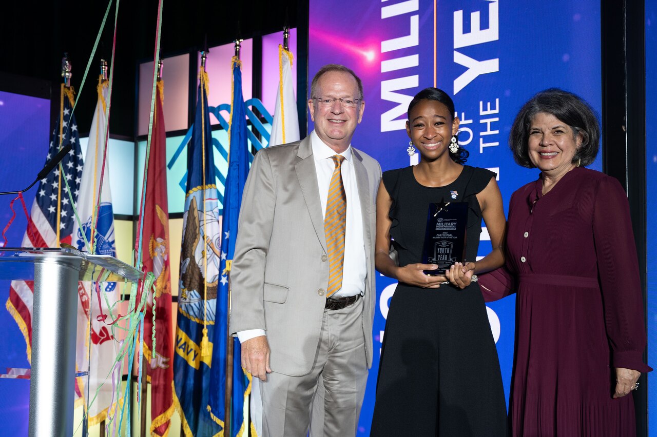 A young woman holds an award and poses for a photo with two other people.