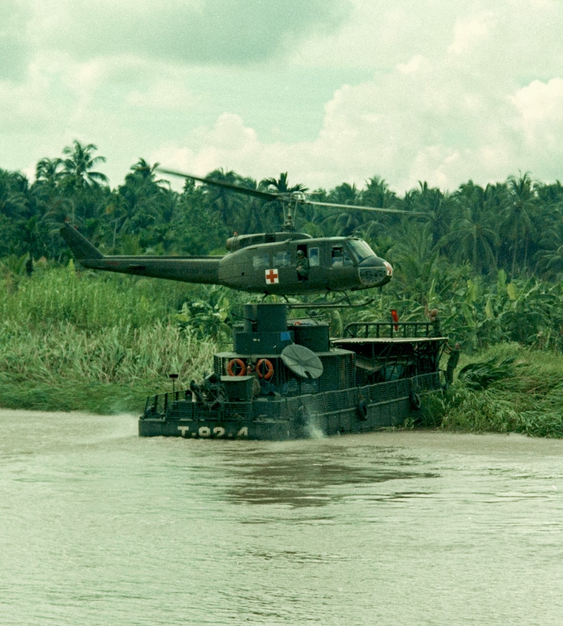 A helicopter lands on a helipad on a small boat beached near a jungle.