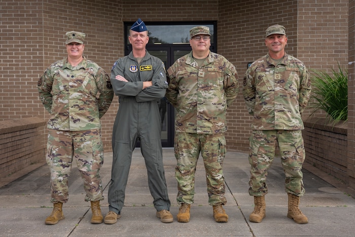 Four military members pose for a photo in front of a building.