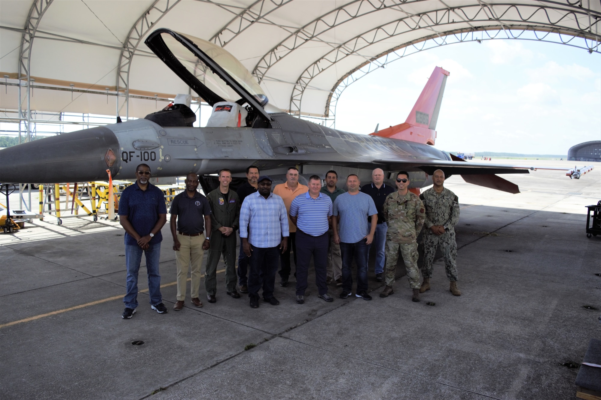 A group of civilian and military personnel stand in front of a plane