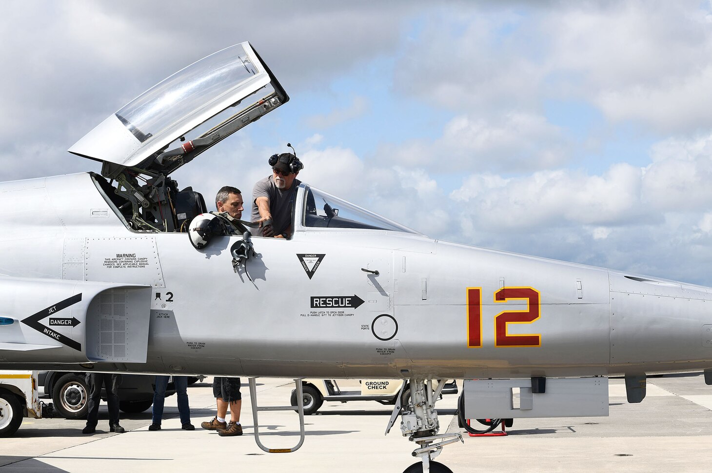 Joe Hawley, a Fleet Readiness Center Southeast (FRCSE) ground check plane captain, assists FRCSE Adversary Production Officer, Cdr. Mitchell Conover, strap in to an F-5 Tiger II. An FCF tests the aircraft and all of its systems to ensure they work properly. (U.S. Navy Photo by Toiete Jackson/Released)
