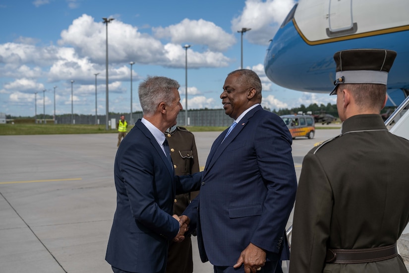 Two men in business suits shake hands at the bottom of a staircase leading down from an aircraft.