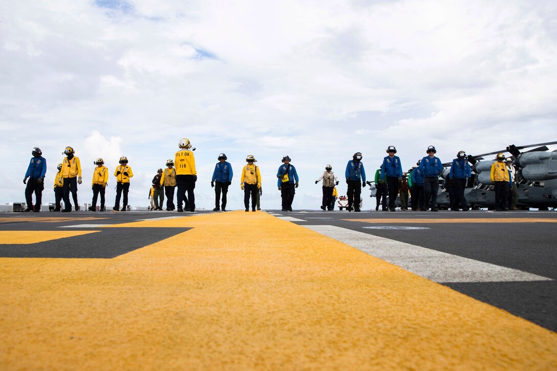 Sailors and Marines walk on a flight deck of a ship near aircraft.