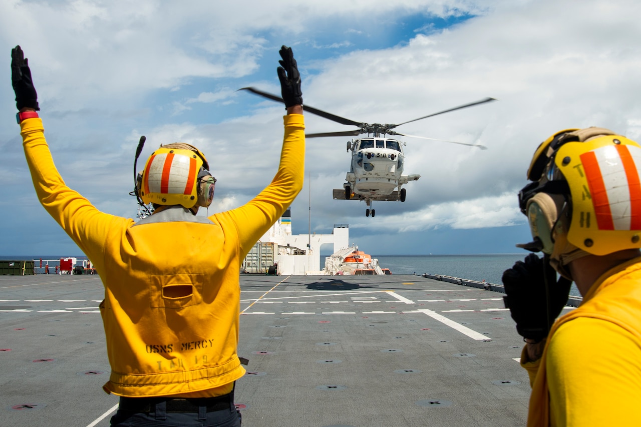A sailor signals to a helicopter aboard a ship at sea.