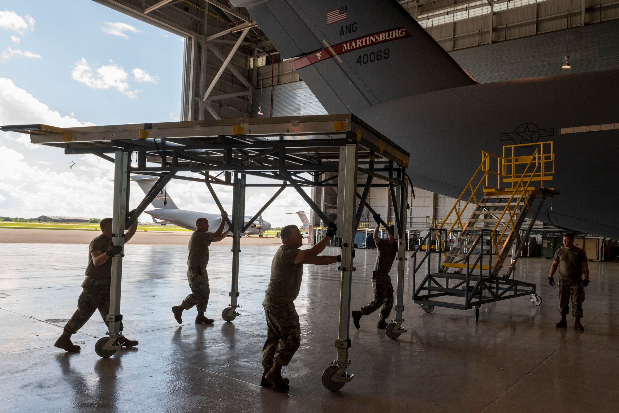 Airmen push maintenance stands in aircraft hangar