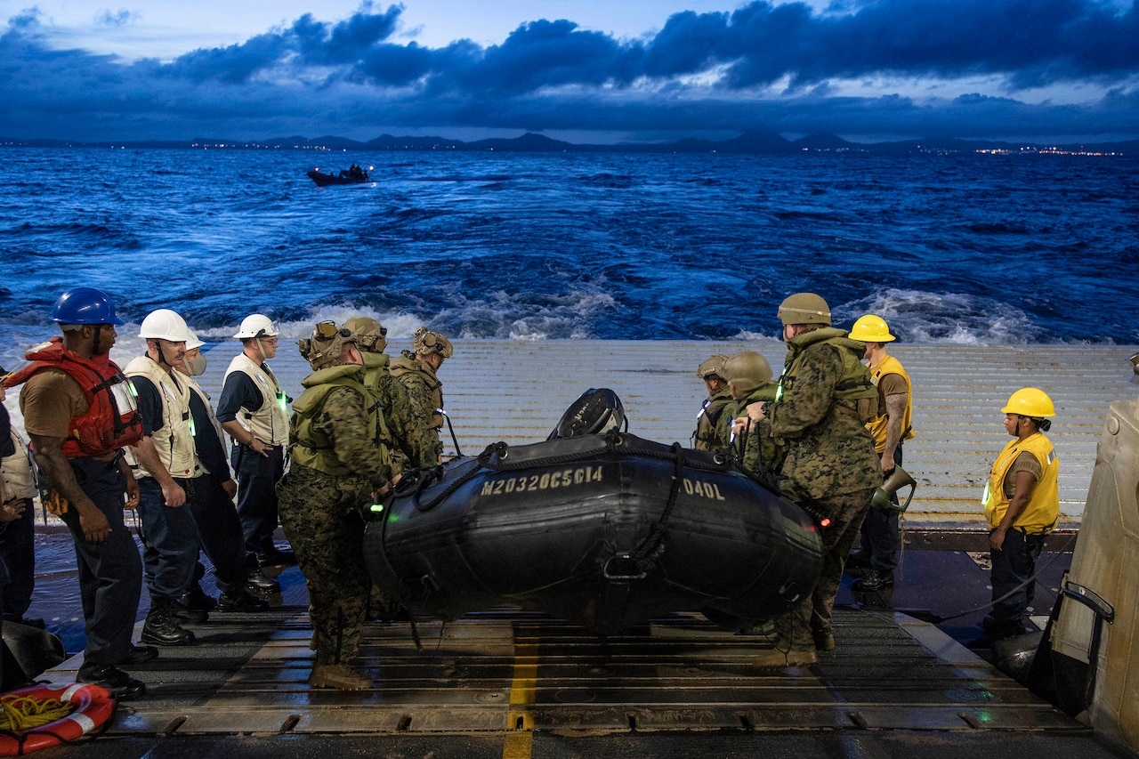 Marines stand on ship deck by a rubber boat.