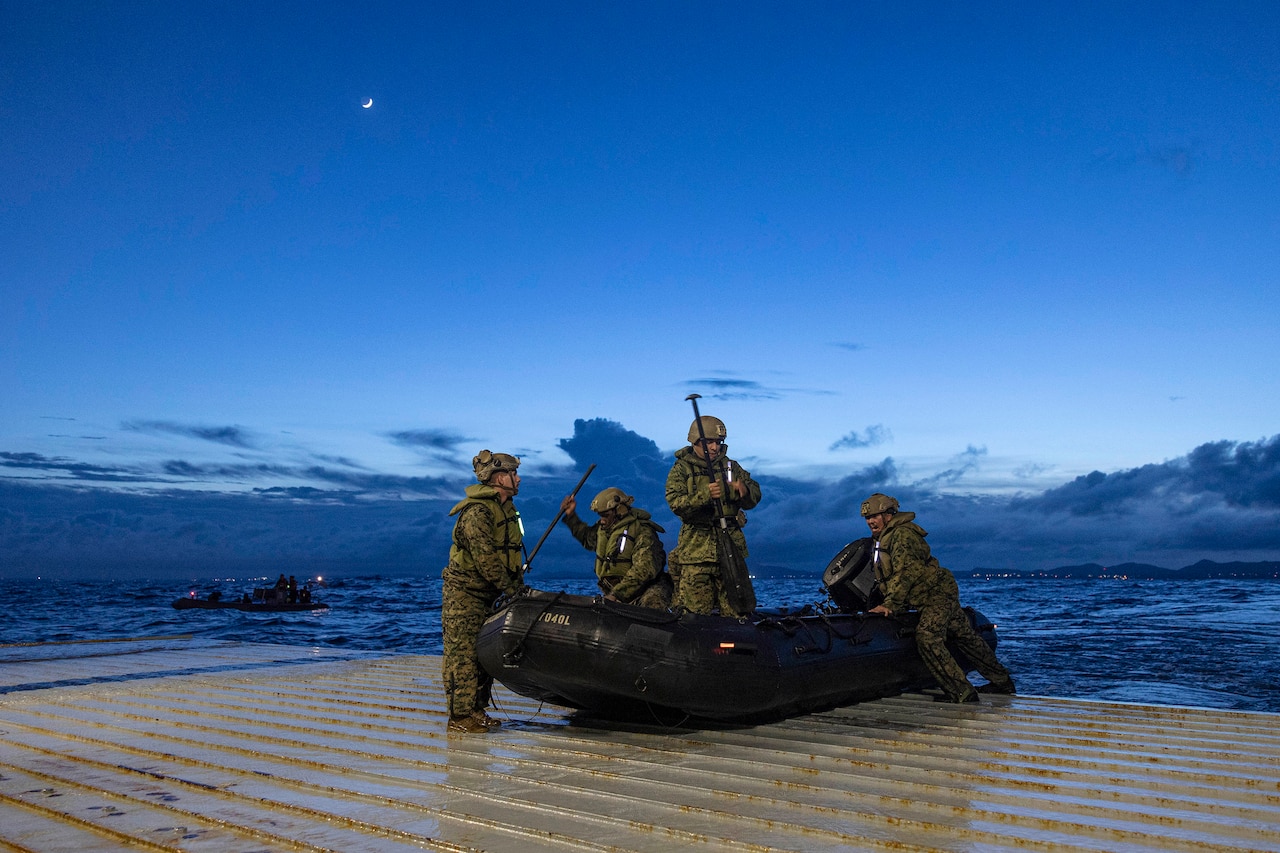 Four Marines get into a rubber boat on a ship's deck at night.