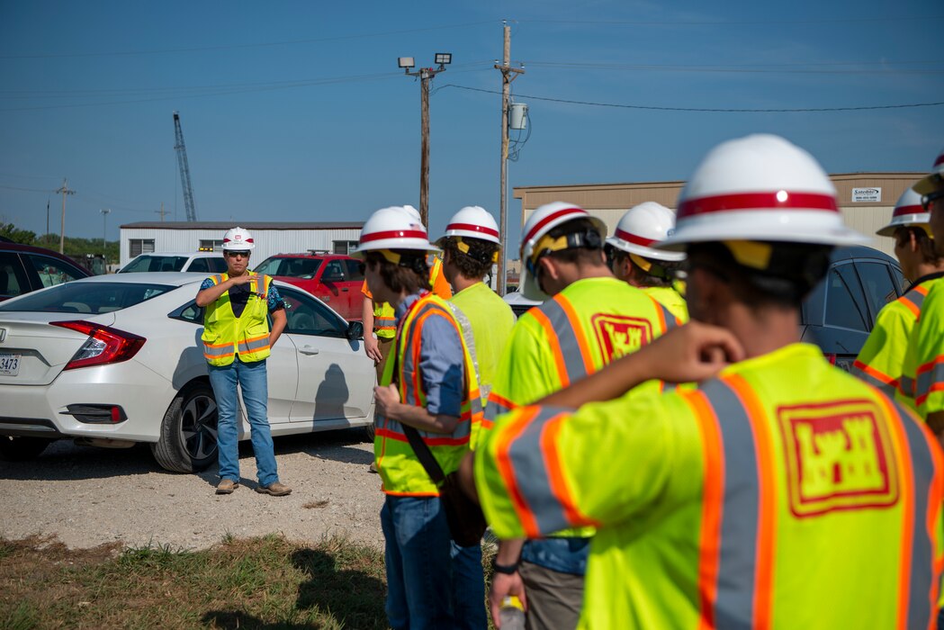 A senior engineer wearing a hard hat and yellow safety vest briefs interns wearing the same thing