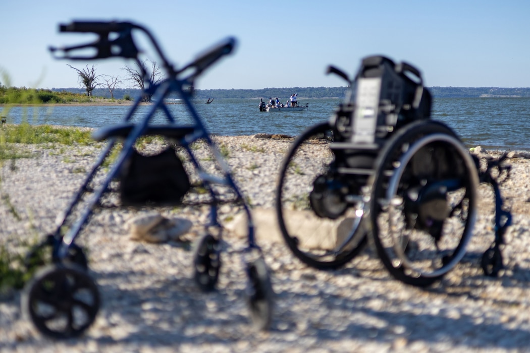 a walker and a wheelchair sit on the shoreline while people fish from a boat in the background