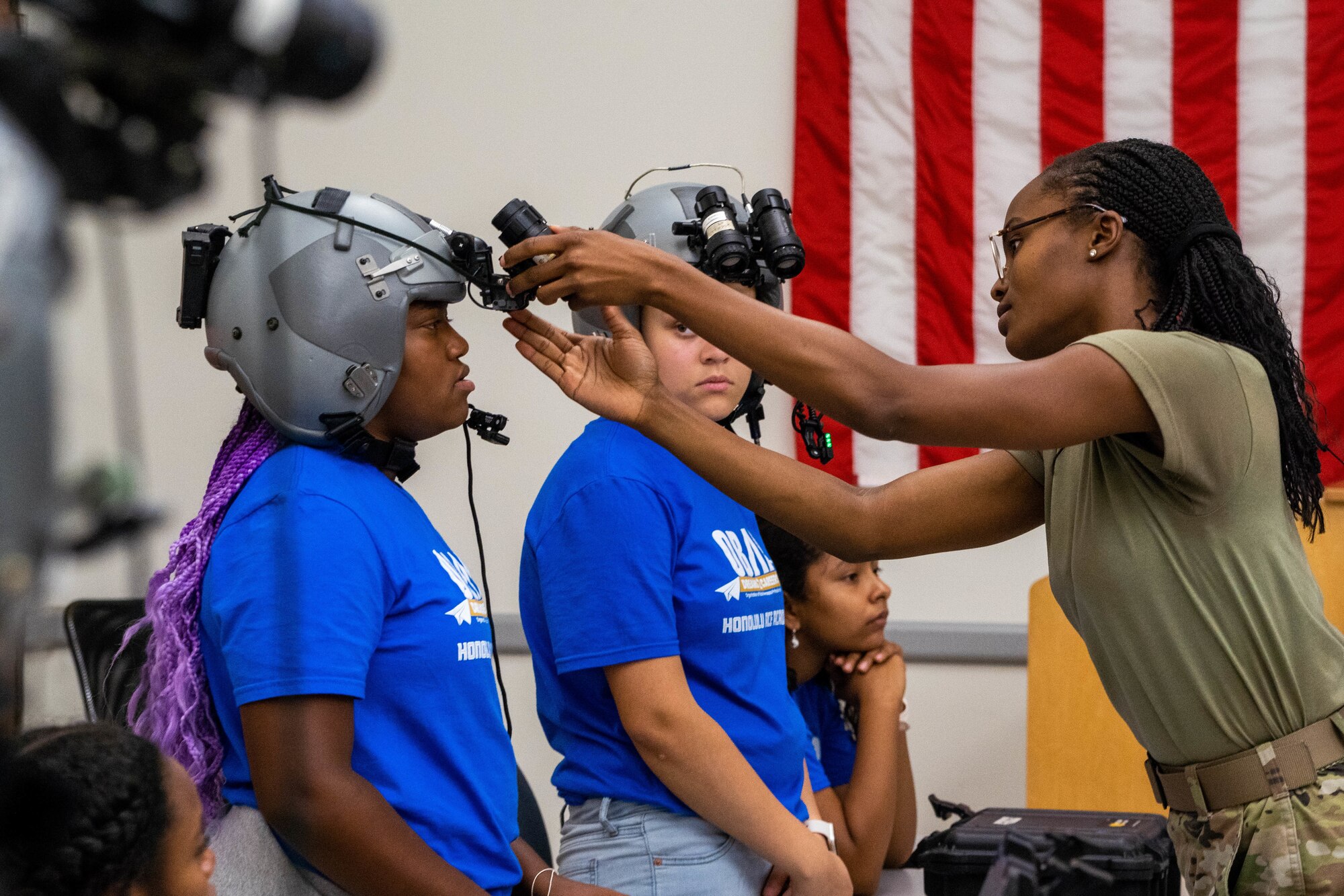 Airman Miya Lyons, 15th Operations Support Squadron aircrew flight equipment apprentice, adjusts night vision goggles on an Organization of Black Aerospace Professionals Aerospace Career Education Academy visitor during a base tour at Joint Base Pearl Harbor-Hickam, Hawaii, July 28, 2022. OBAP provides kids between the ages of 13-18 different opportunities in aerospace by supporting, mentoring and educating members and communities. (U.S. Air Force photo by Senior Airman Makensie Cooper)